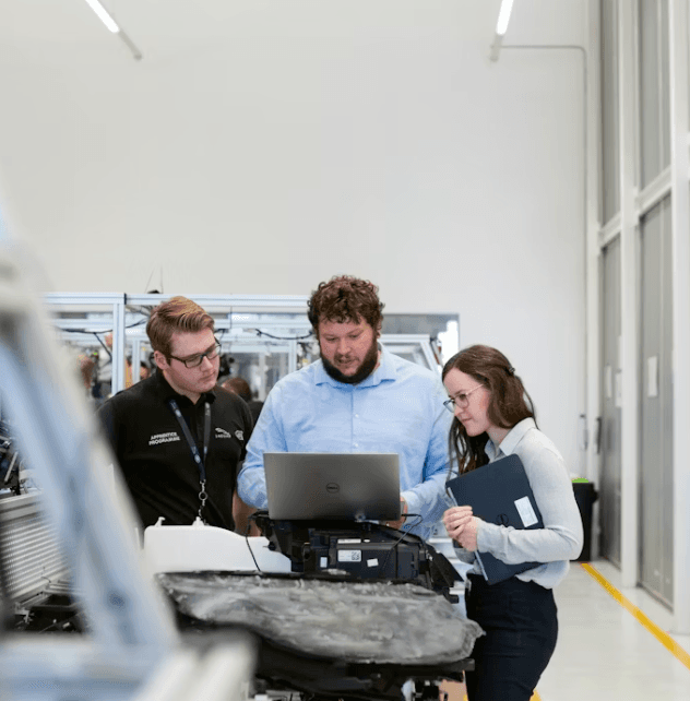 Three people in automotive workshop looking at laptop - team collaboration