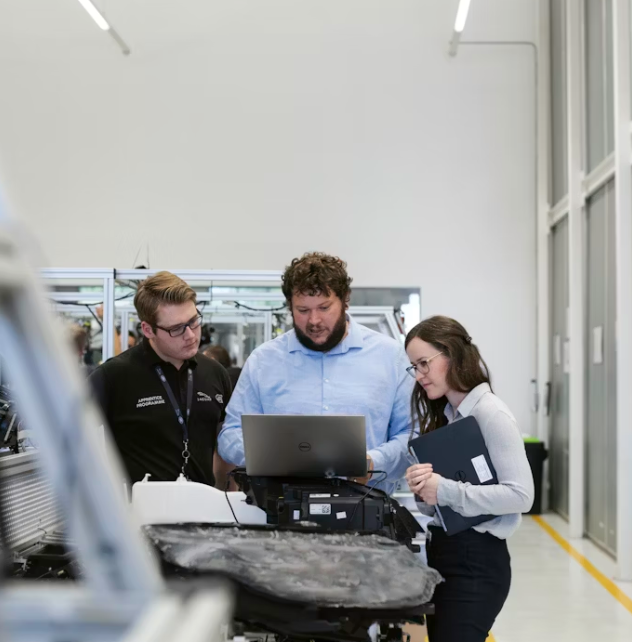 Three people in automotive workshop looking at laptop - team collaboration